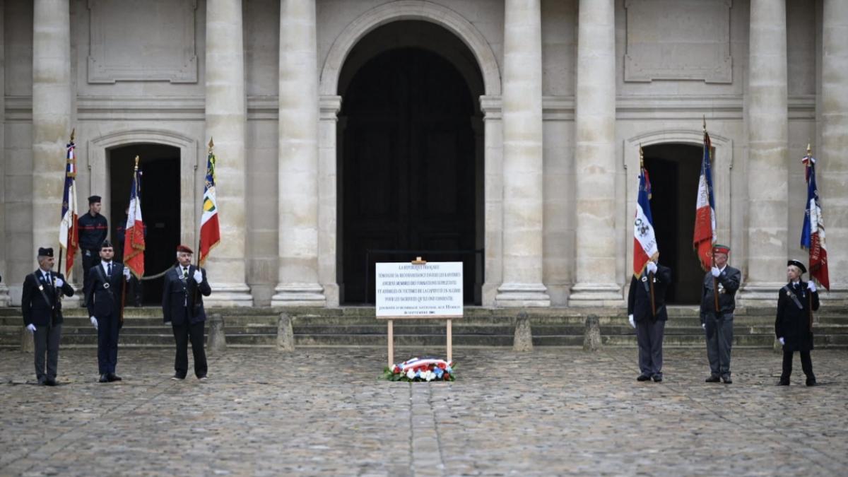 Des porte-drapeaux d'associations d'anciens combattants et de Harkis entourent une plaque en l'honneur des Harkis dans la cour d’honneur des Invalides